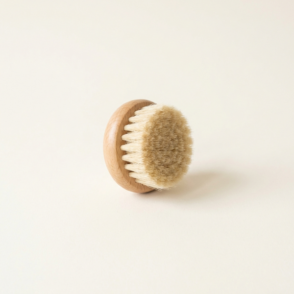 Brosse lymphatique visage en bois clair à poils naturels, sur fond crème